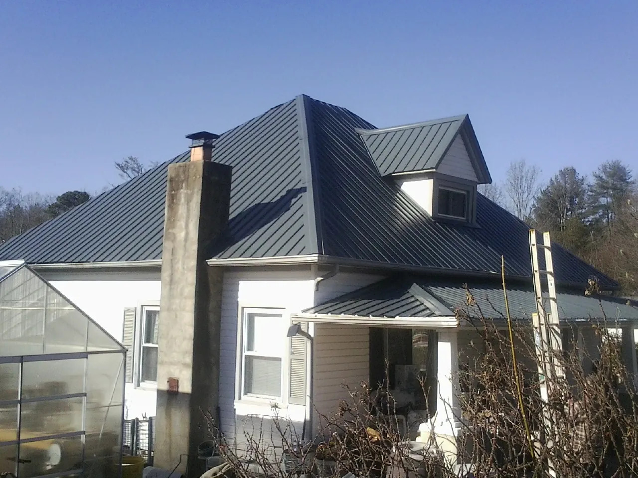 Dark blue standing seam metal roof on a white farmhouse with dormer — Slate & Tile Roof Repair by Roofing Brothers in Springtown