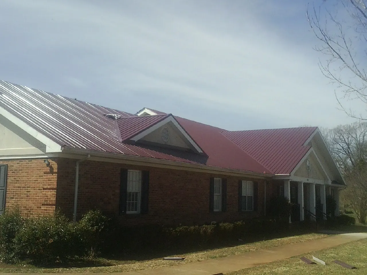 Red metal roof with gabled entries on a long brick building, from a Hail Damage Roof Repair job in Springtown