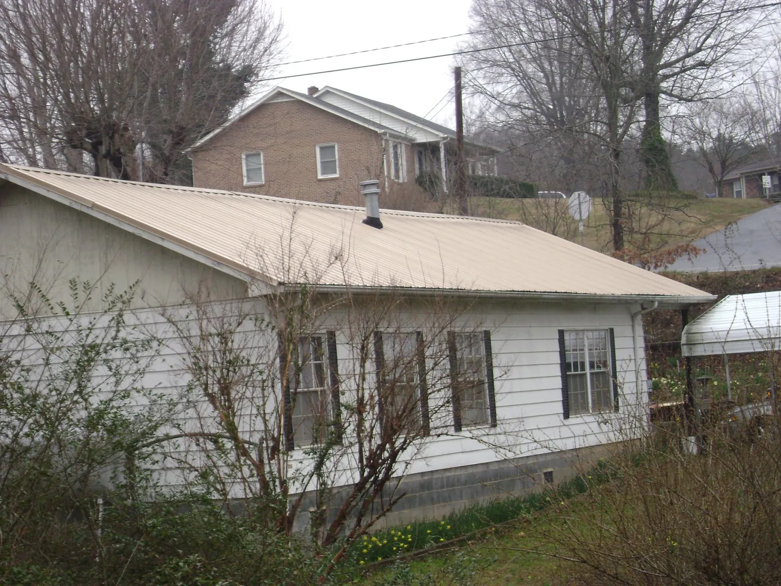 Tan metal roof on a white sided house set into a hillside — Commercial Roofing by Roofing Brothers in Springtown
