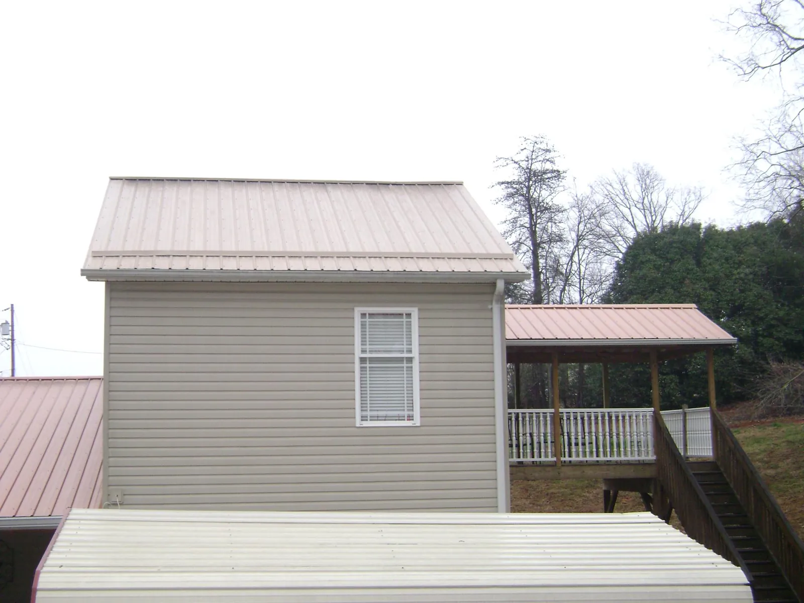 Tan metal roofs on a two story addition and attached porch, from a Roof Replacement job in Springtown